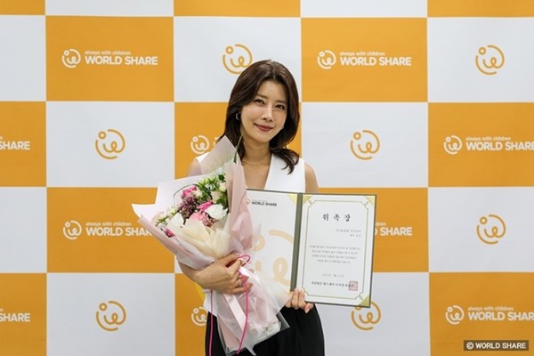 사진 설명/유선 친선대사가 위촉장을 들고 환히 웃고 있다.